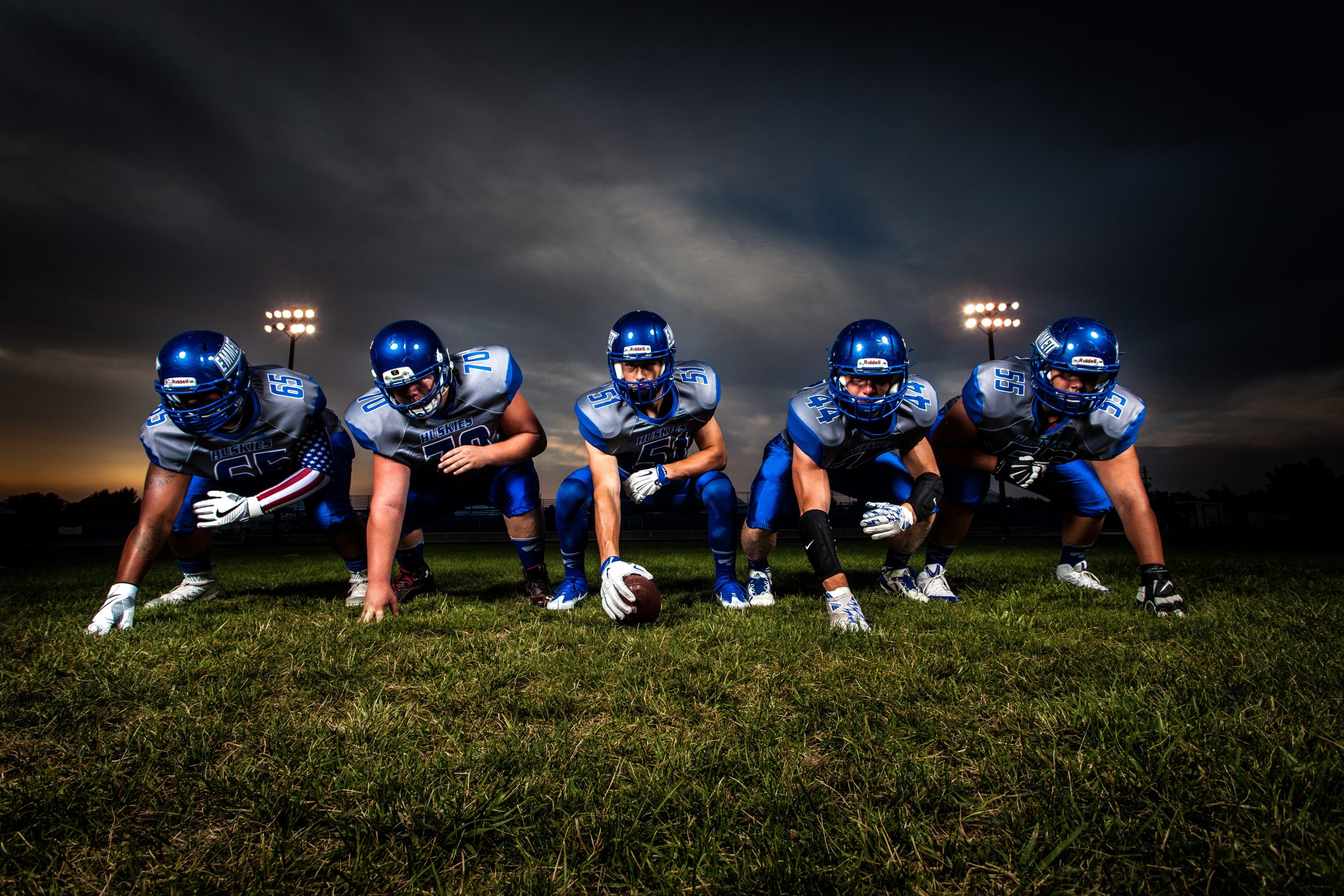 Fünf American-Football-Spieler in Startposition auf dem Spielfeld bei Flutlicht
