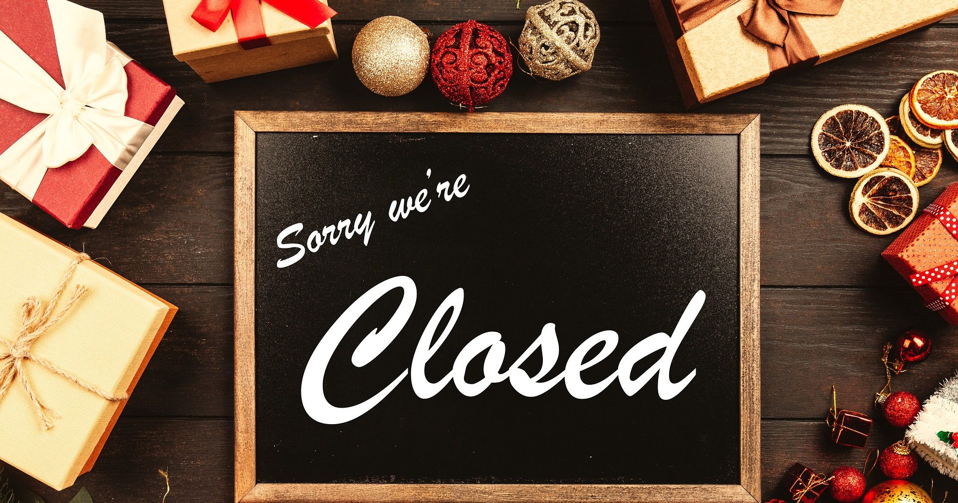 Tafel mit der Aufschrift „Sorry we're closed“, umgeben von Weihnachtsdeko und Geschenken