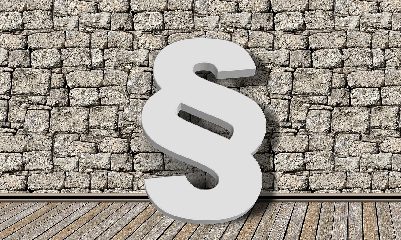 Graues Paragrafenzeichen vor Steinwand und Holzboden