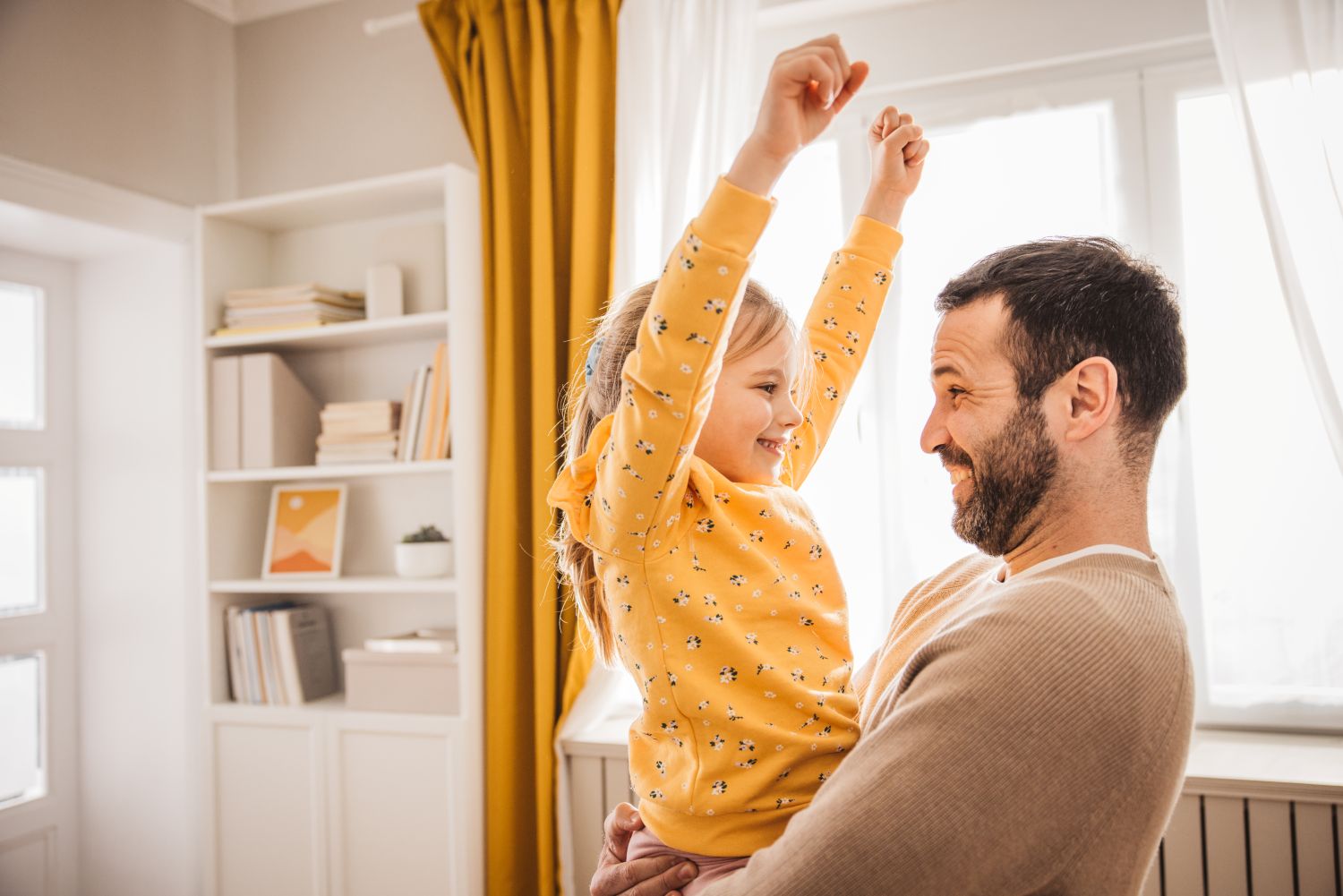 Vater hält seine Tochter in den Arm, die glücklich ihre Arme nach oben wirft.