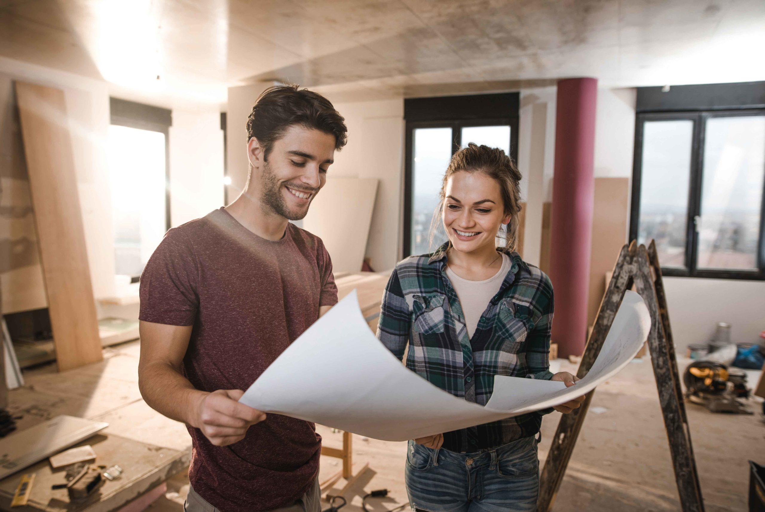 Junge glückliche Paar Baupläne selbst auf Baustelle in ihrer Wohnung zu prüfen